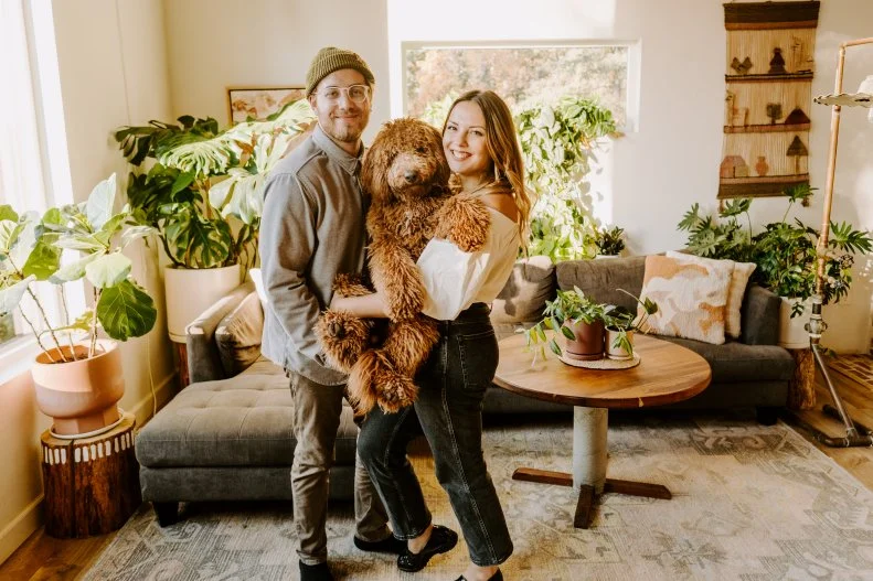 Couple Stands In Living Room of Custom Cabin in Alaska Holding Dog